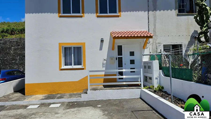 Fachada branca com molduras amarelas e telhado de telha
